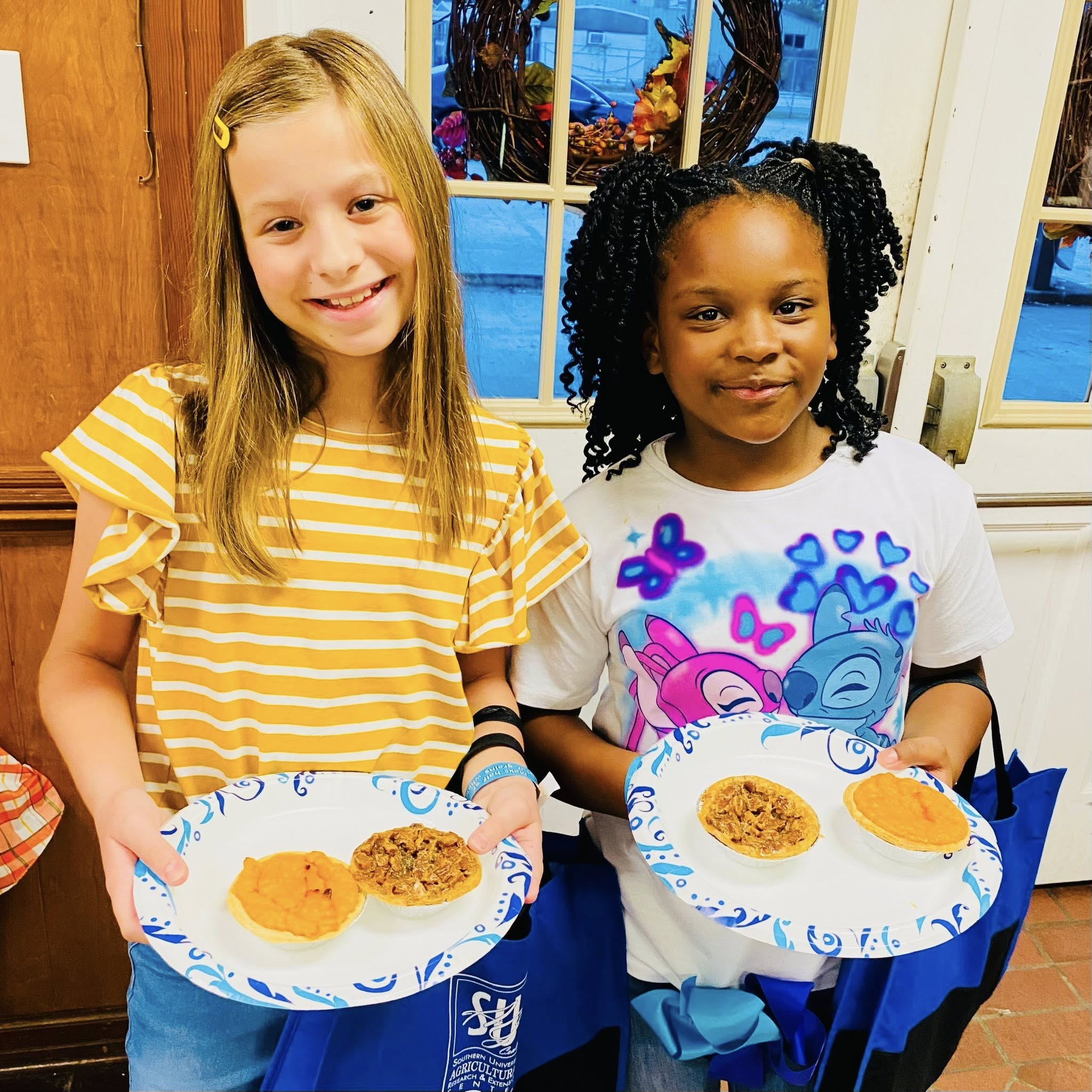 Two girls holding plates with mini pies on them.